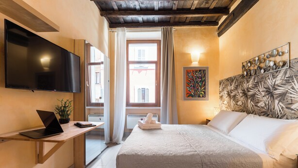 Une chambre d’hôtel avec un lit, un bureau avec un ordinateur portable, un téléviseur à écran plat et une fenêtre avec des rideaux.