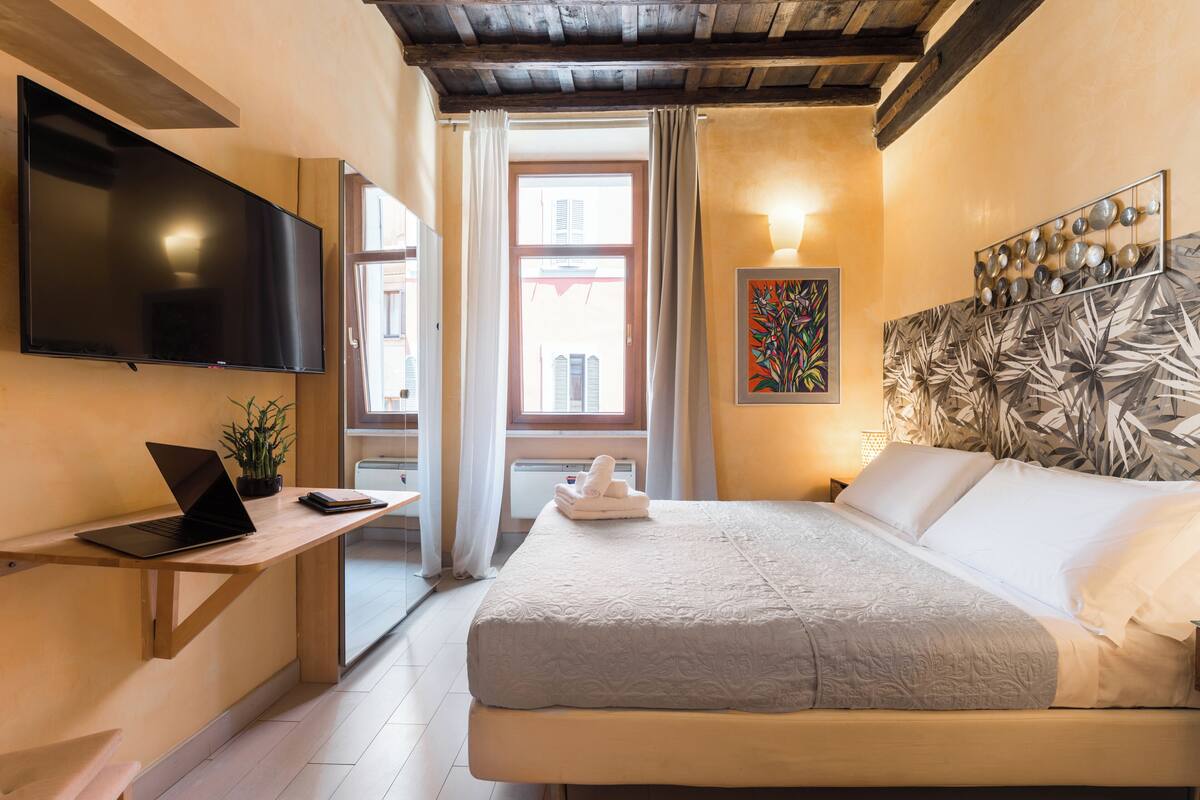 Ein Hotelzimmer mit Bett, Schreibtisch, Laptop, Flachbildfernseher und einem Fenster mit Vorhängen.