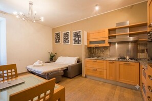 A compact bedroom with a bed, a desk, and a chair, adjacent to a kitchenette with wooden cabinets and stainless steel appliances. - TrinitaDeiMonti Guest House (Rome)