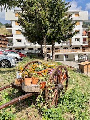 A modern building with balconies, a parking area, and a cart with potted plants. - Hotel Hermitage (Sestriere)