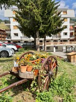 Un edificio moderno con balcones, un área de estacionamiento y un carrito con plantas en macetas.