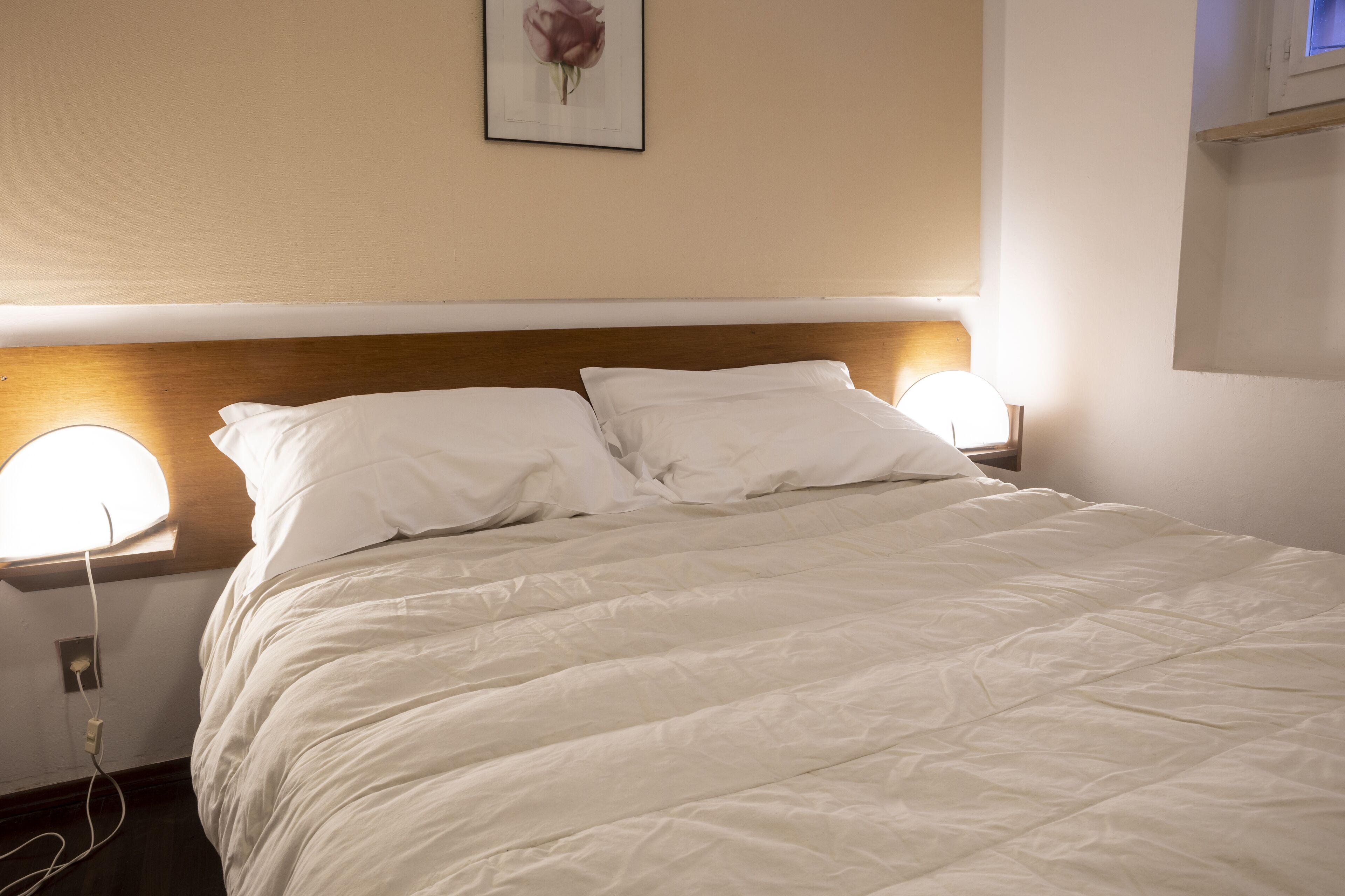 A neatly made bed with white linens, two bedside lamps, and a framed picture on the wall.