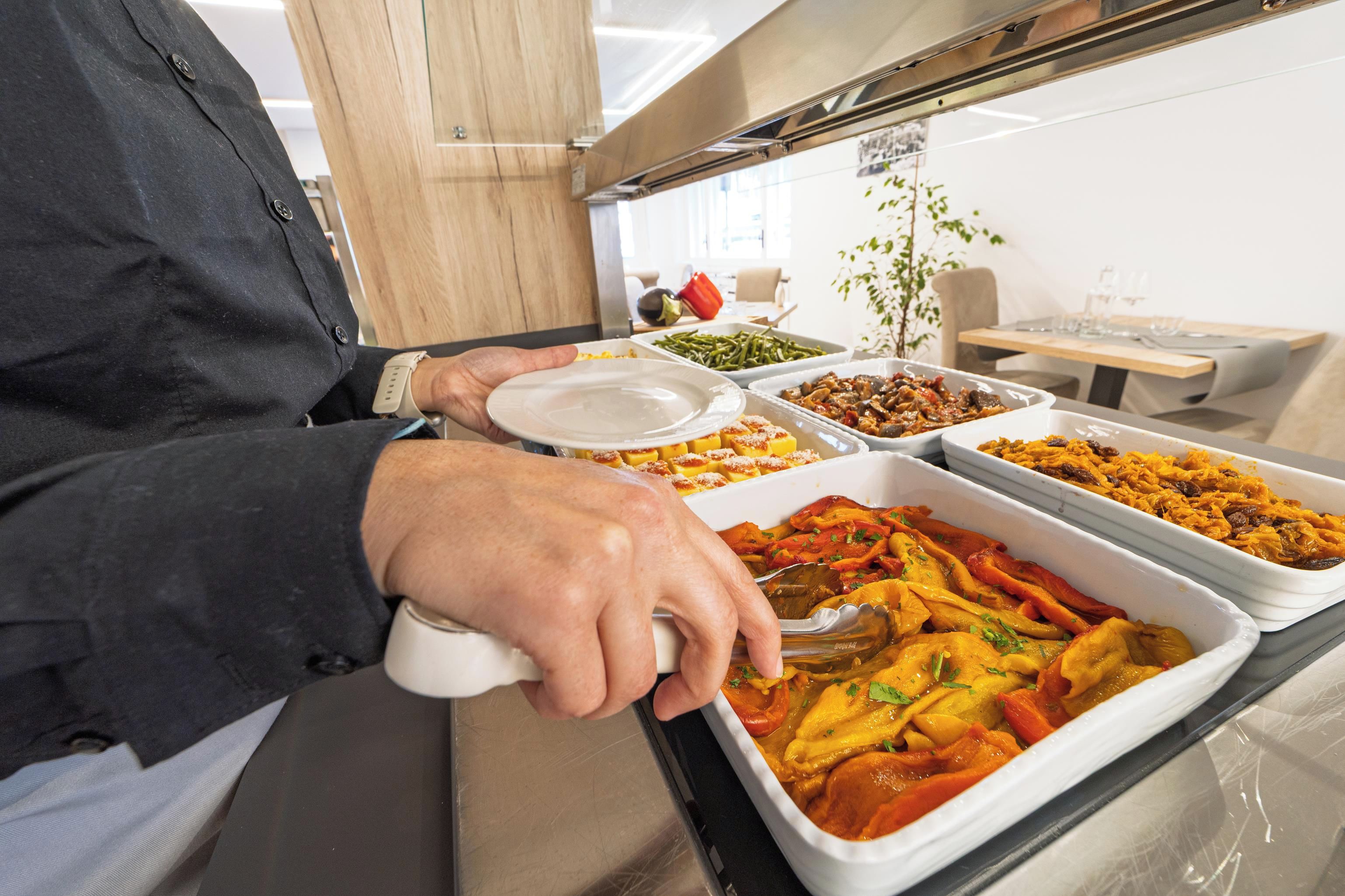 A buffet setup with various dishes in trays, including a section with red vegetables and another with a yellow dish.