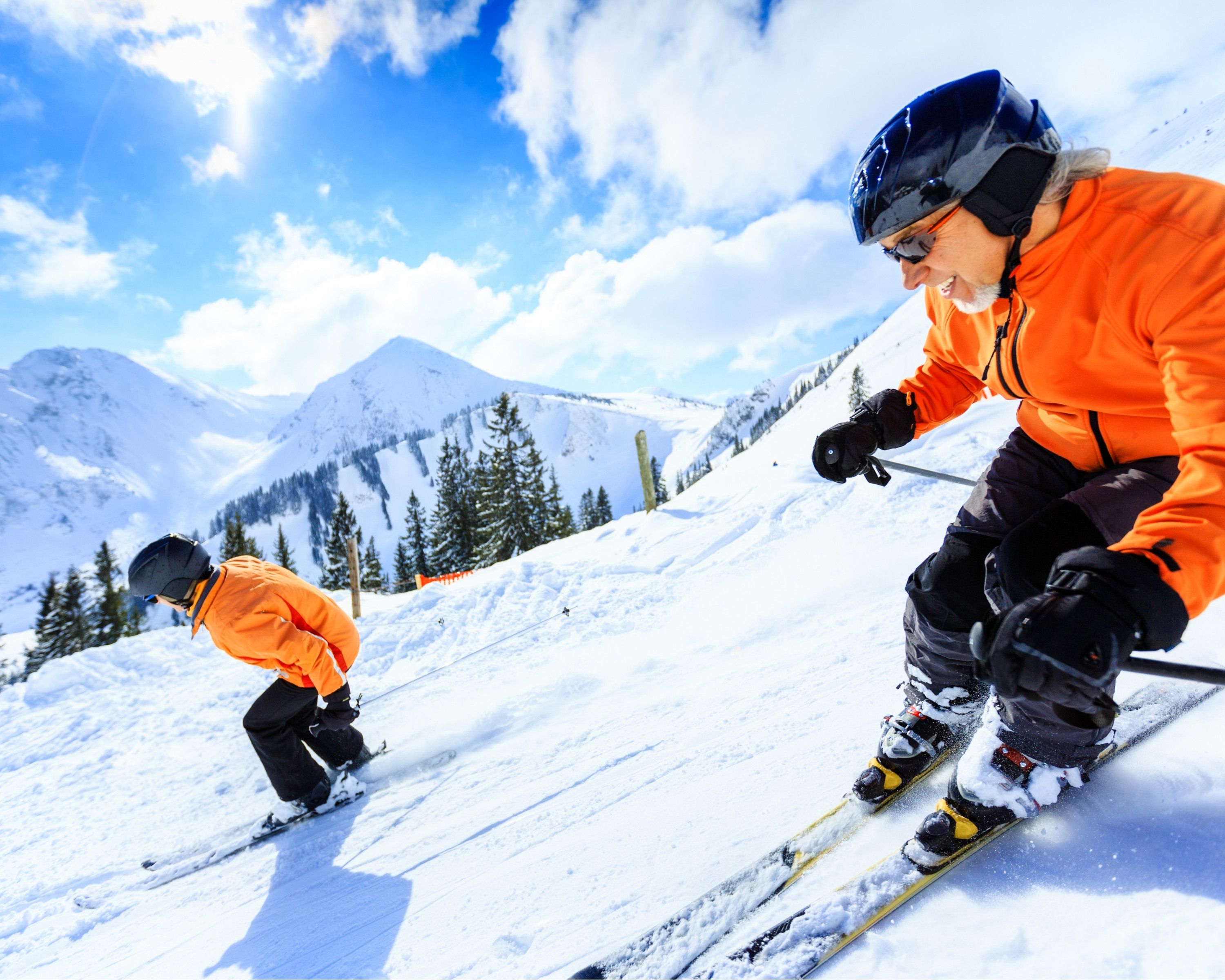Eine verschneite Berglandschaft mit Skifahrern in orangefarbenen Jacken.