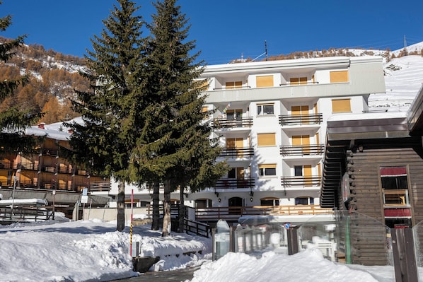 A multi-story building with balconies and a ski slope in the background.