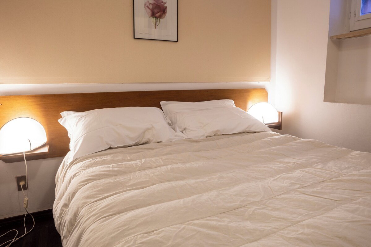 A neatly made bed with white linens, two bedside lamps, and a framed picture on the wall.
