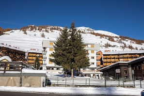 Un hotel de varios pisos, con un árbol destacado al frente y una montaña nevada al fondo.