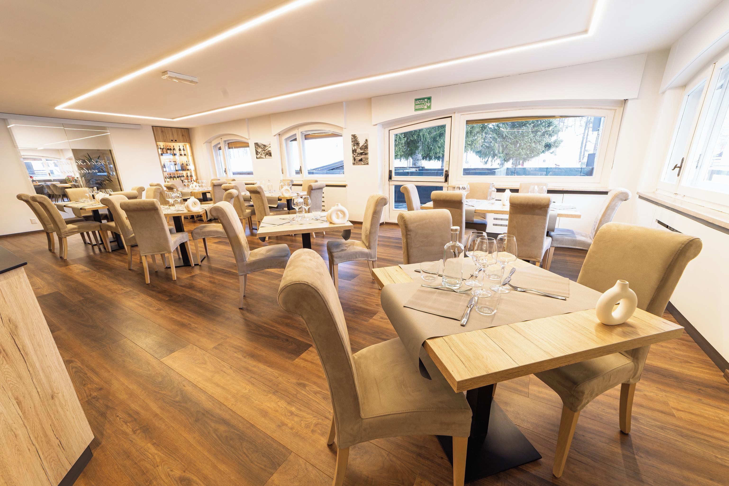A restaurant with wooden flooring, beige upholstered chairs, and tables set for dining.