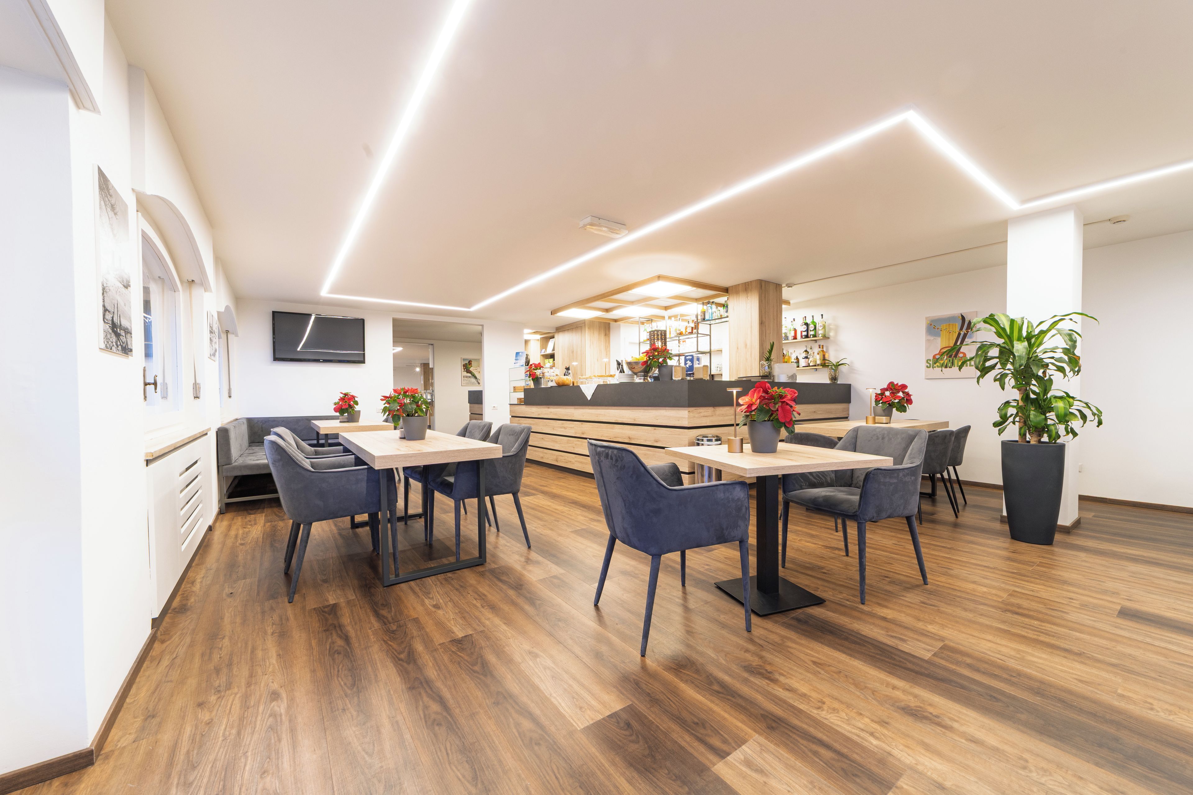 A modern dining area with wooden flooring, grey upholstered chairs, and a central table with a vase of flowers.