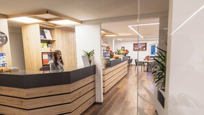 A reception area with a wooden reception desk, a clock on the wall, and a counter with various items. - Hotel Hermitage (Sestriere)