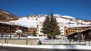 A hotel with multiple floors, a ski slope in the background, and a prominent tree in the foreground. - Hotel Hermitage (Sestriere)