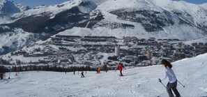 A snow-covered ski slope with skiers and a town in the background. - Hotel Hermitage (Sestriere)