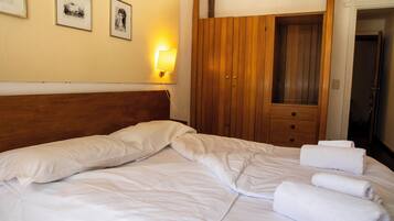 A hotel room with a bed, a wooden wardrobe, and a wall-mounted light.