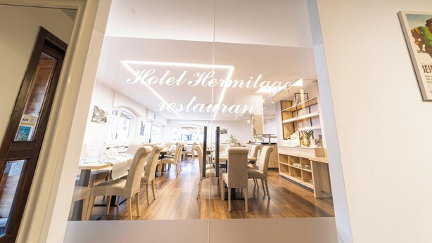 A modern restaurant with a bright interior, wooden flooring, and a central dining area with tables and chairs. - Hotel Hermitage (Sestriere)