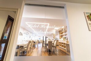 A modern restaurant with a bright interior, wooden flooring, and a central dining area with tables and chairs.