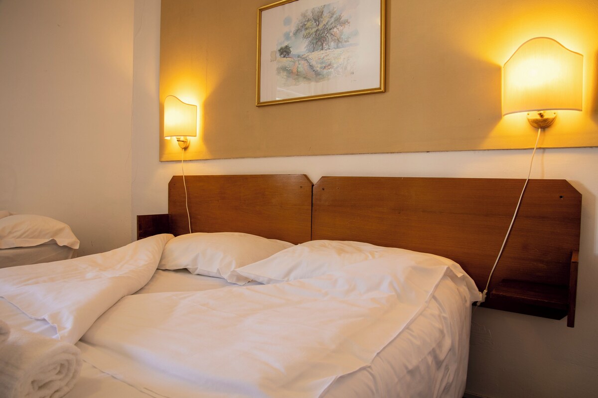 A neatly made bed with white linens, a wooden headboard, and two wall-mounted lamps.