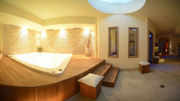 A spa area with a large hot tub, wooden benches, and a stone wall. - Vittoria (Folgaria)