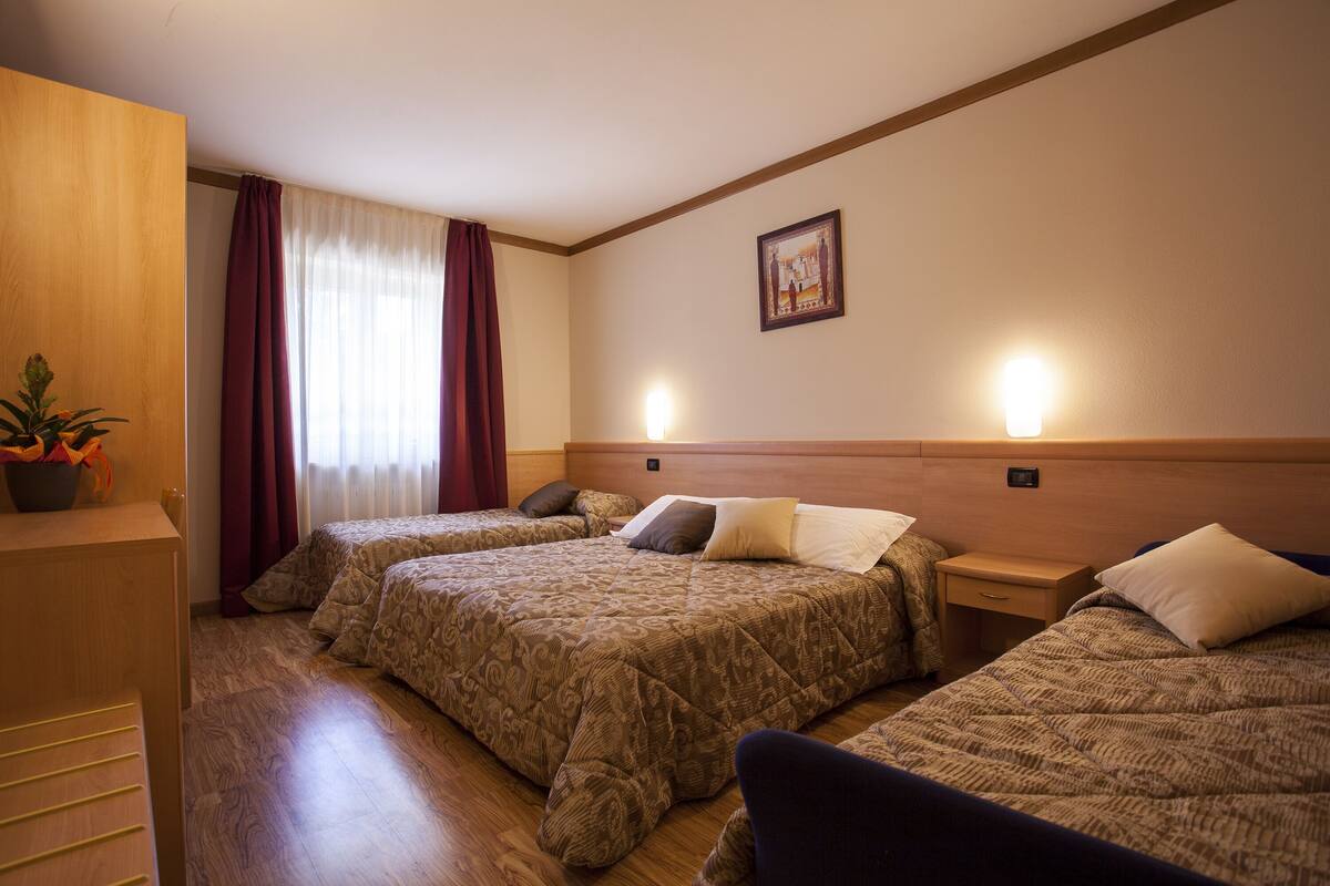 A hotel room with two beds, wooden flooring, a nightstand, a lamp, and a painting on the wall.