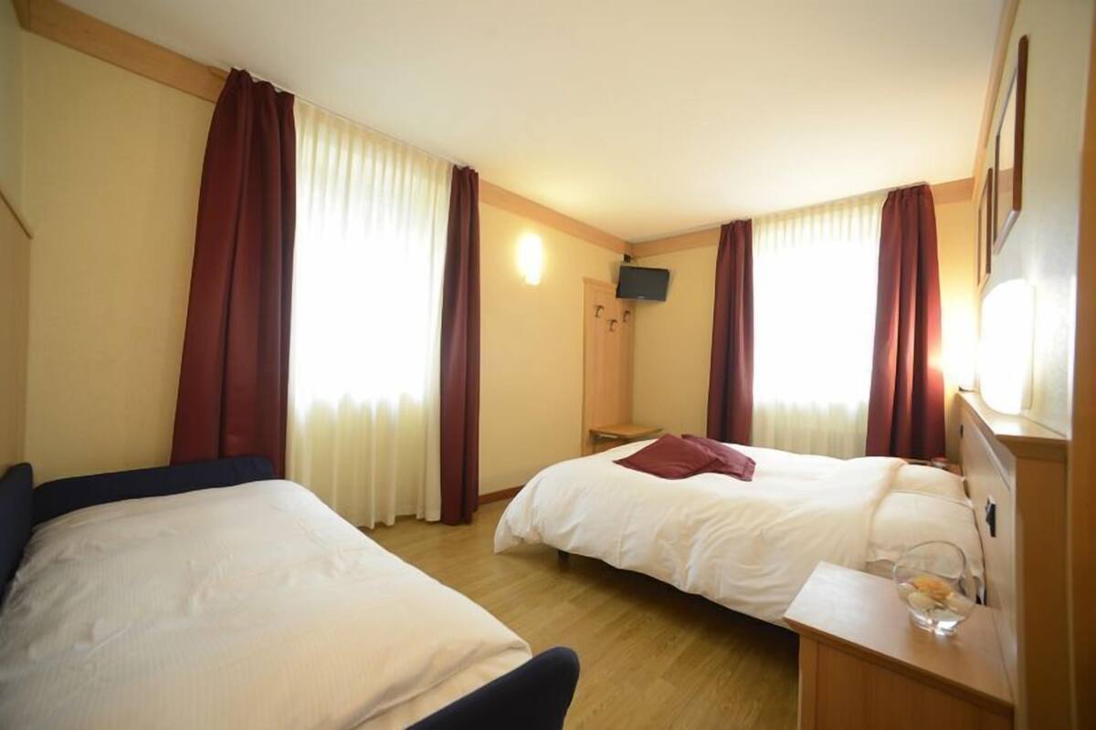 A hotel room with two beds, a flat-screen TV mounted on the wall, and a small table with a glass of water.