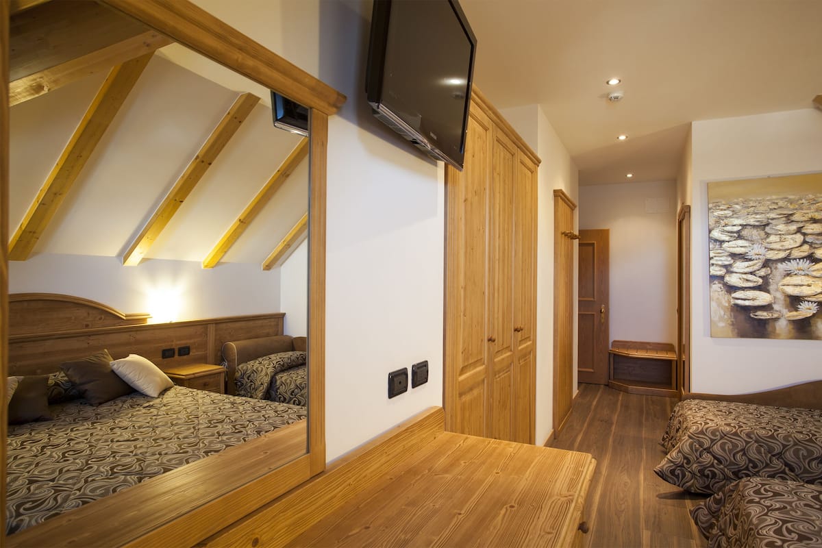 A bedroom with a sloped ceiling, wooden furniture, a flat-screen TV, and a painting on the wall.