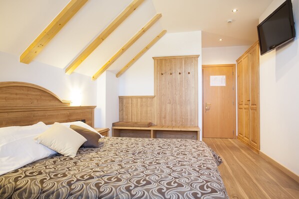 A bedroom with a wooden bed, a wardrobe, and a television mounted on the wall. - Vittoria (Folgaria)