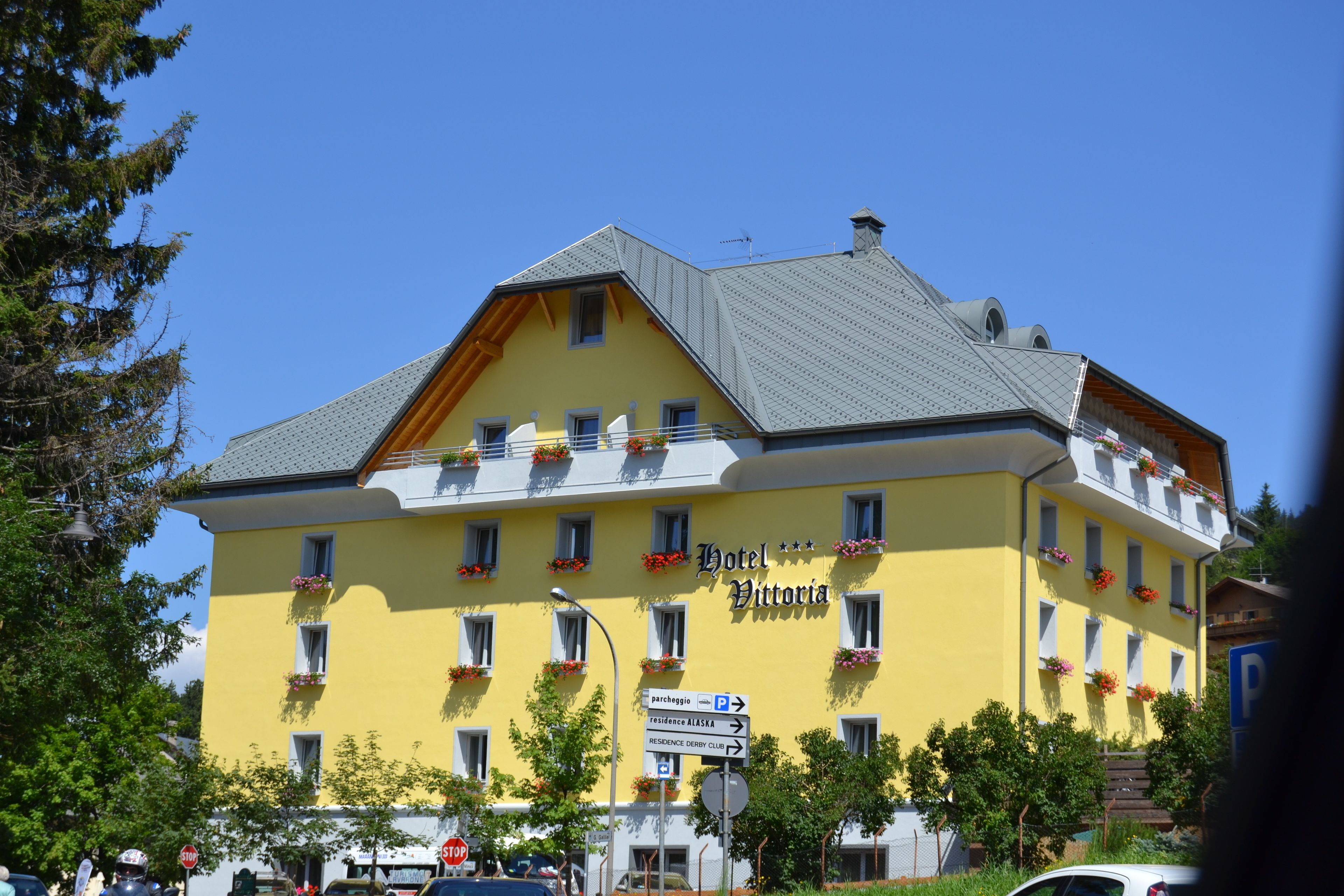 A yellow building with a sign reading "Hotel Vittoria" and a parking sign below it.