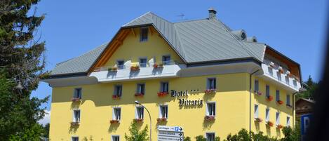 A yellow building with a sign reading "Hotel Vittoria" and a parking sign below it.
