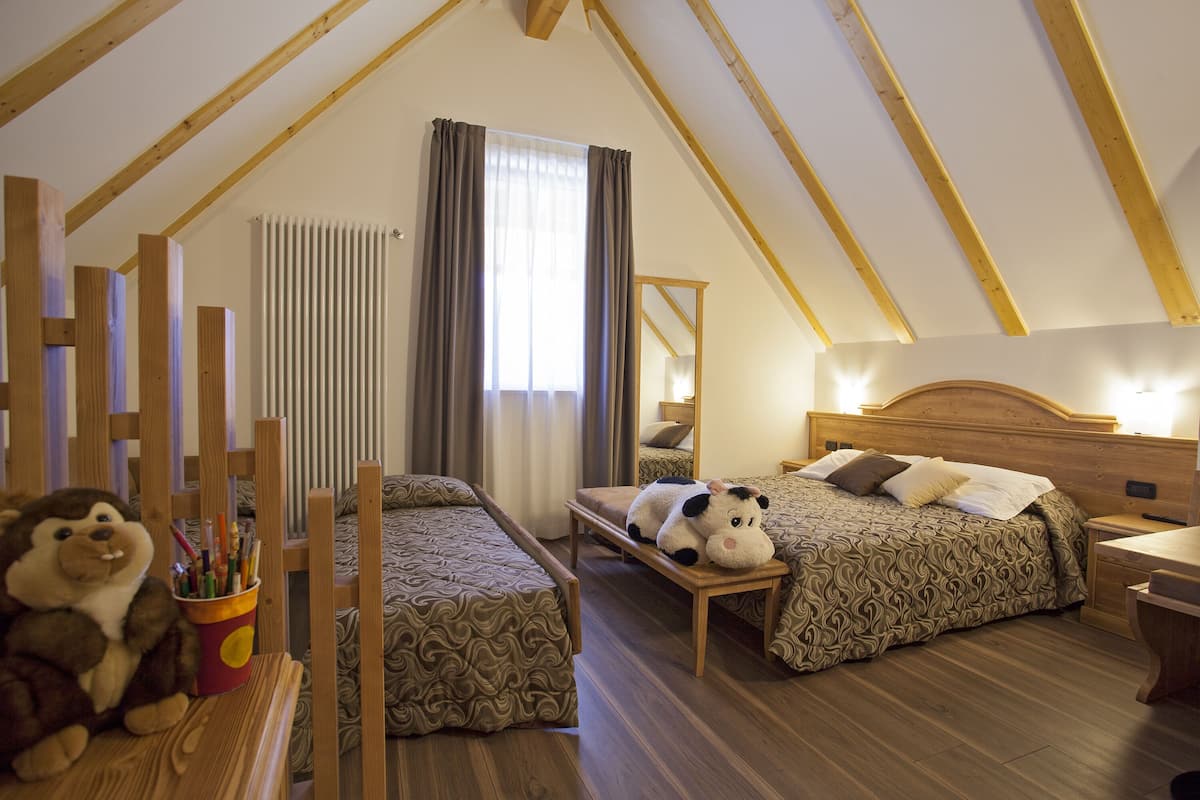 A cozy attic bedroom with two beds, wooden beams, a large window with curtains, and a stuffed animal on the left side.
