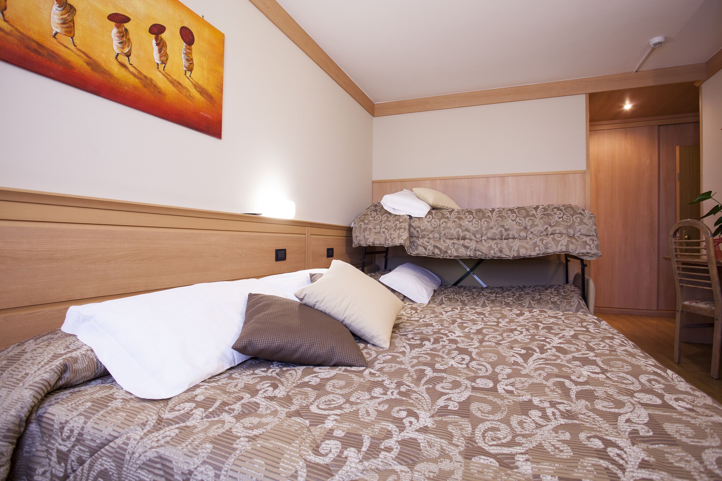 A bedroom with a large bed, a smaller bed, a wooden headboard, a painting on the wall, and a chair.