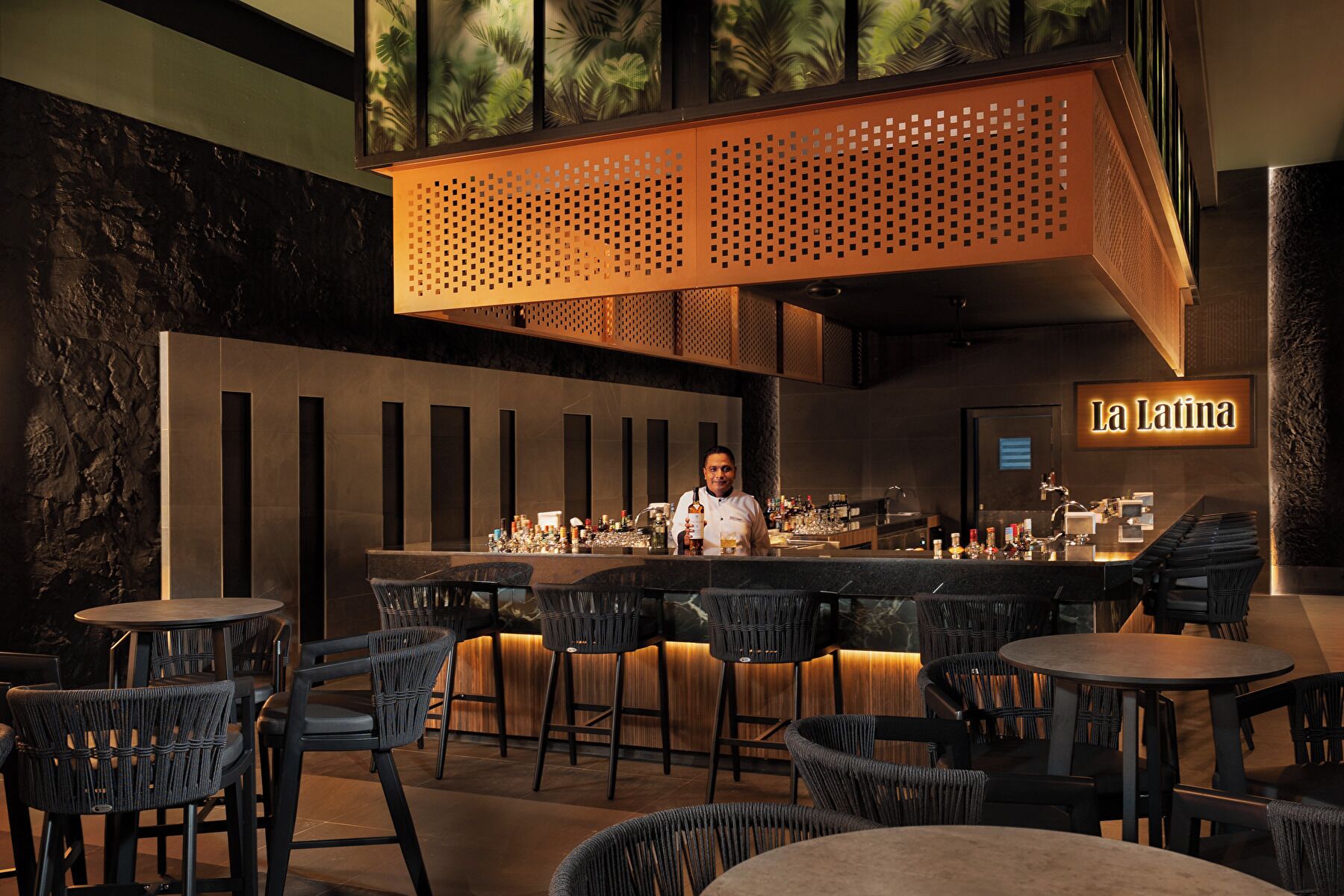 A bar area with a chef, bar stools, and a sign reading 'La Latina'.