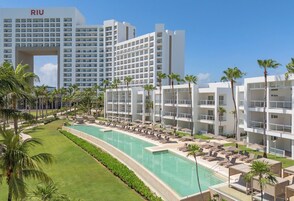 Um hotel com piscina, várias varandas e palmeiras.