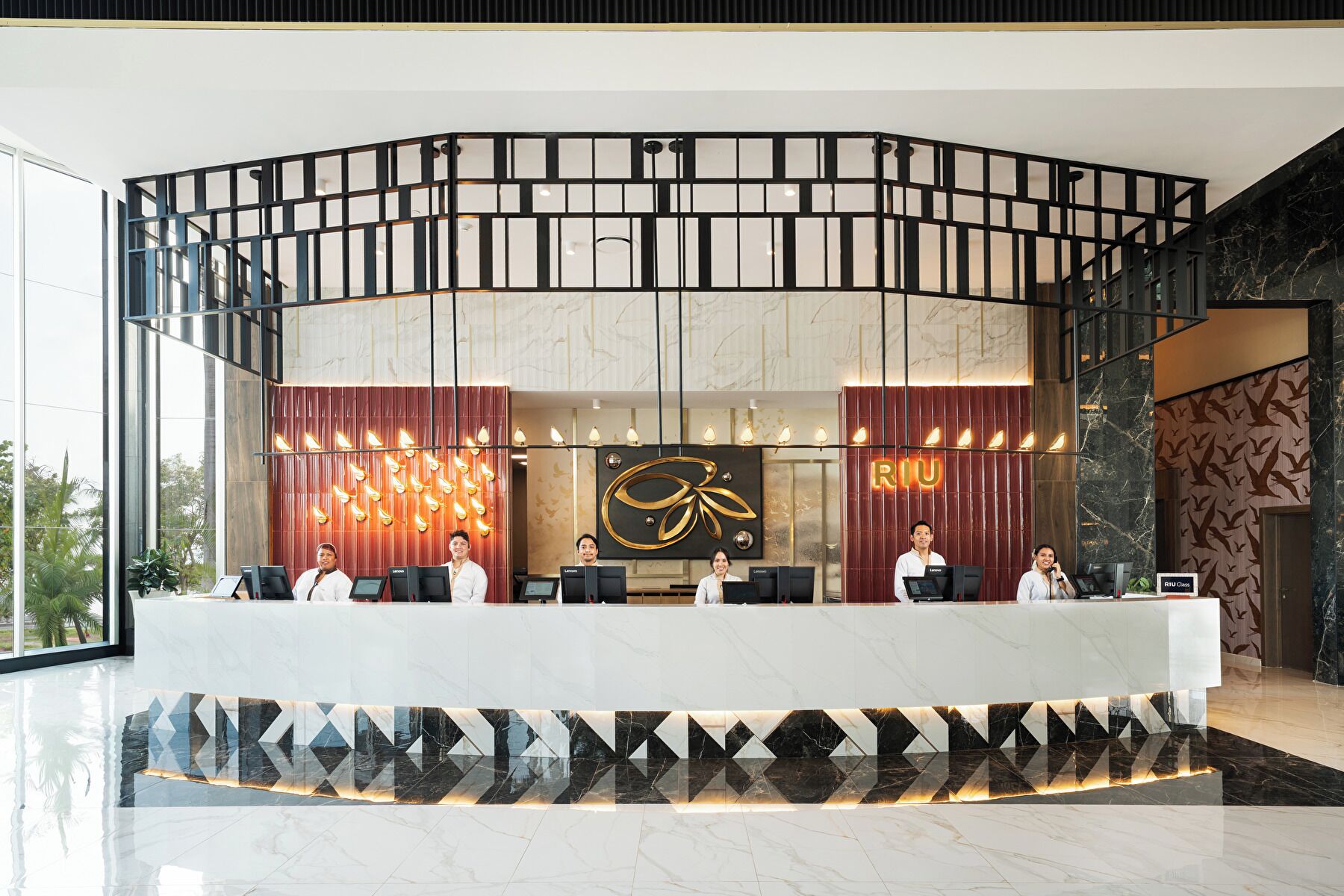 A hotel reception area with a modern design, featuring a curved reception desk, a large decorative wall, and a seating area for guests.