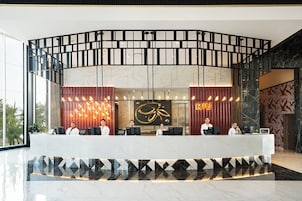 Zona de recepción de un hotel con diseño moderno, que incluye un mostrador curvo, un gran panel decorativo y un área de descanso para huéspedes.