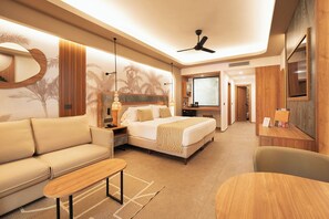Una habitación de hotel con una cama, un sofá, un escritorio, un ventilador de techo y un televisor.