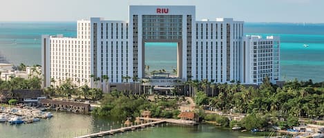 A large hotel with a prominent central entrance, surrounded by a marina with boats and a clear view of the ocean.