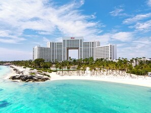 Un hotel grande con un arco central, rodeado por una playa y palmeras.