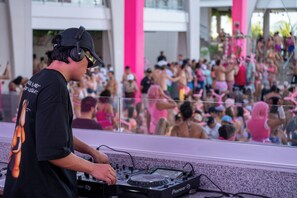 Une table de DJ équipée d’une console Pioneer, une foule en arrière-plan et une colonne rose.
