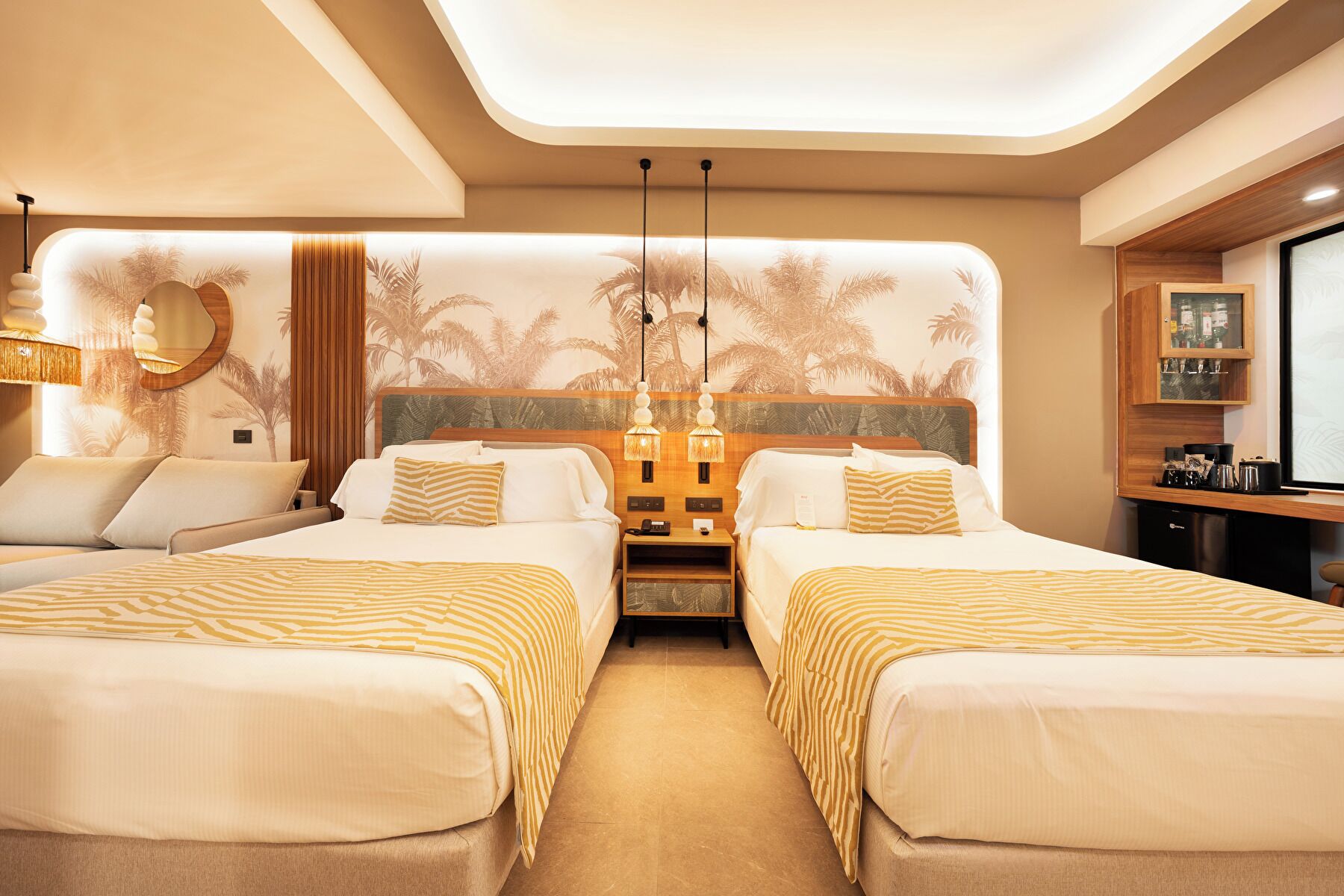 A hotel room with two beds, a nightstand, a desk with a computer, and a minibar.