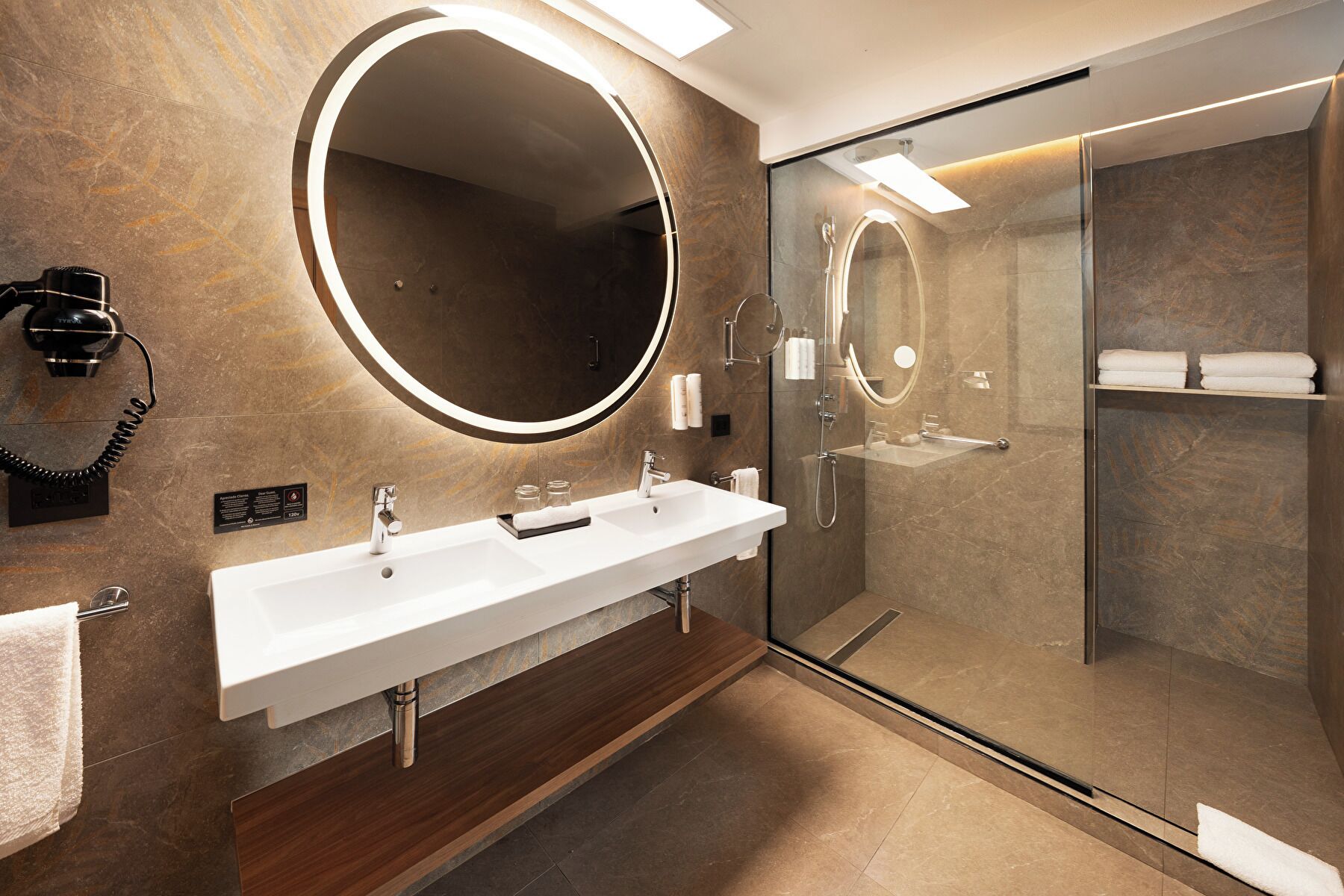 Un baño moderno con un espejo grande, un lavabo blanco y cabina de ducha con paredes de vidrio.