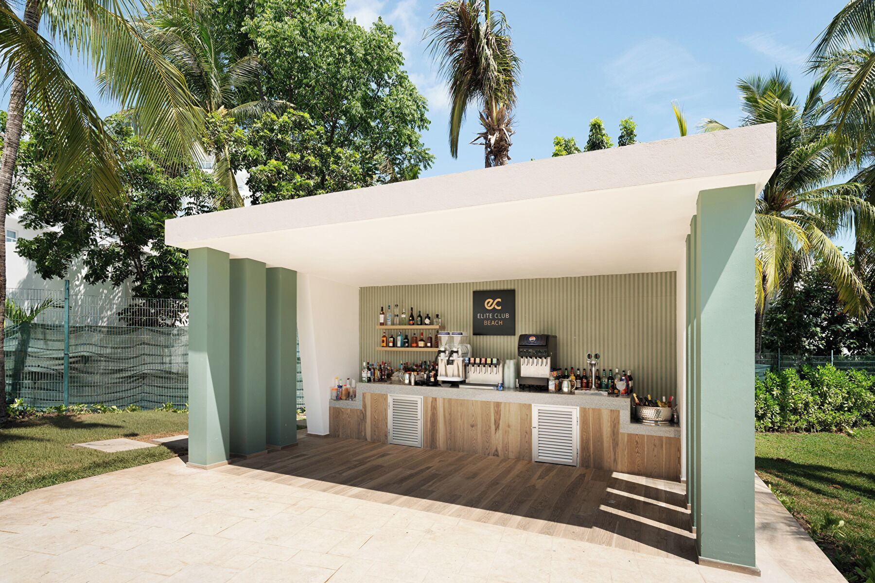 Un área de bar al aire libre con mostrador, taburetes y una variedad de botellas y vasos.