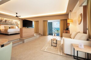 Habitación de hotel moderna con cama, televisor de pantalla plana, balcón con vistas y zona de estar con una mesa de centro.