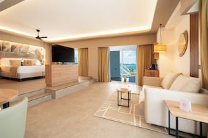 Habitación de hotel moderna con cama, televisor de pantalla plana, balcón con vistas y zona de estar con una mesa de centro.