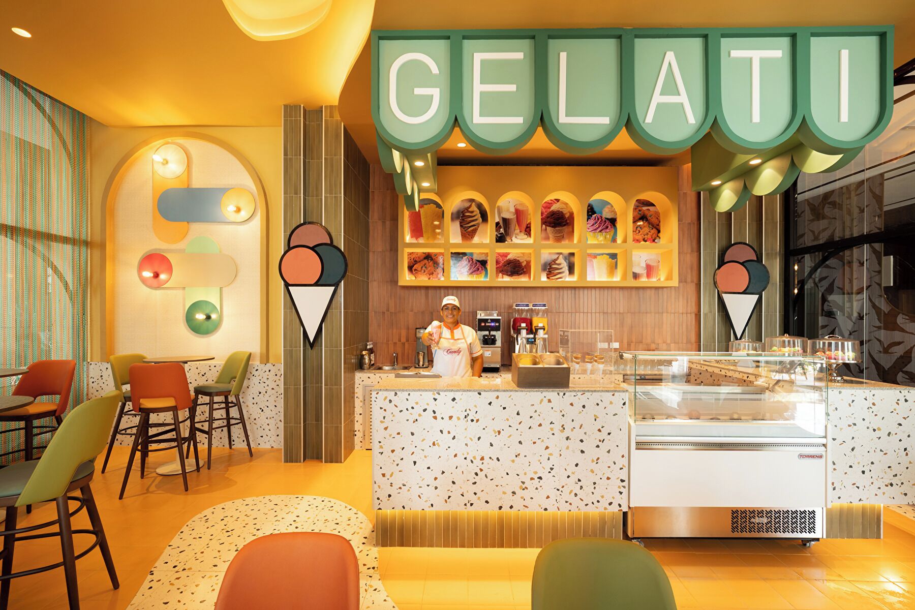 A gelato shop with a colorful interior, a counter with a gelato display, and a seating area with chairs.