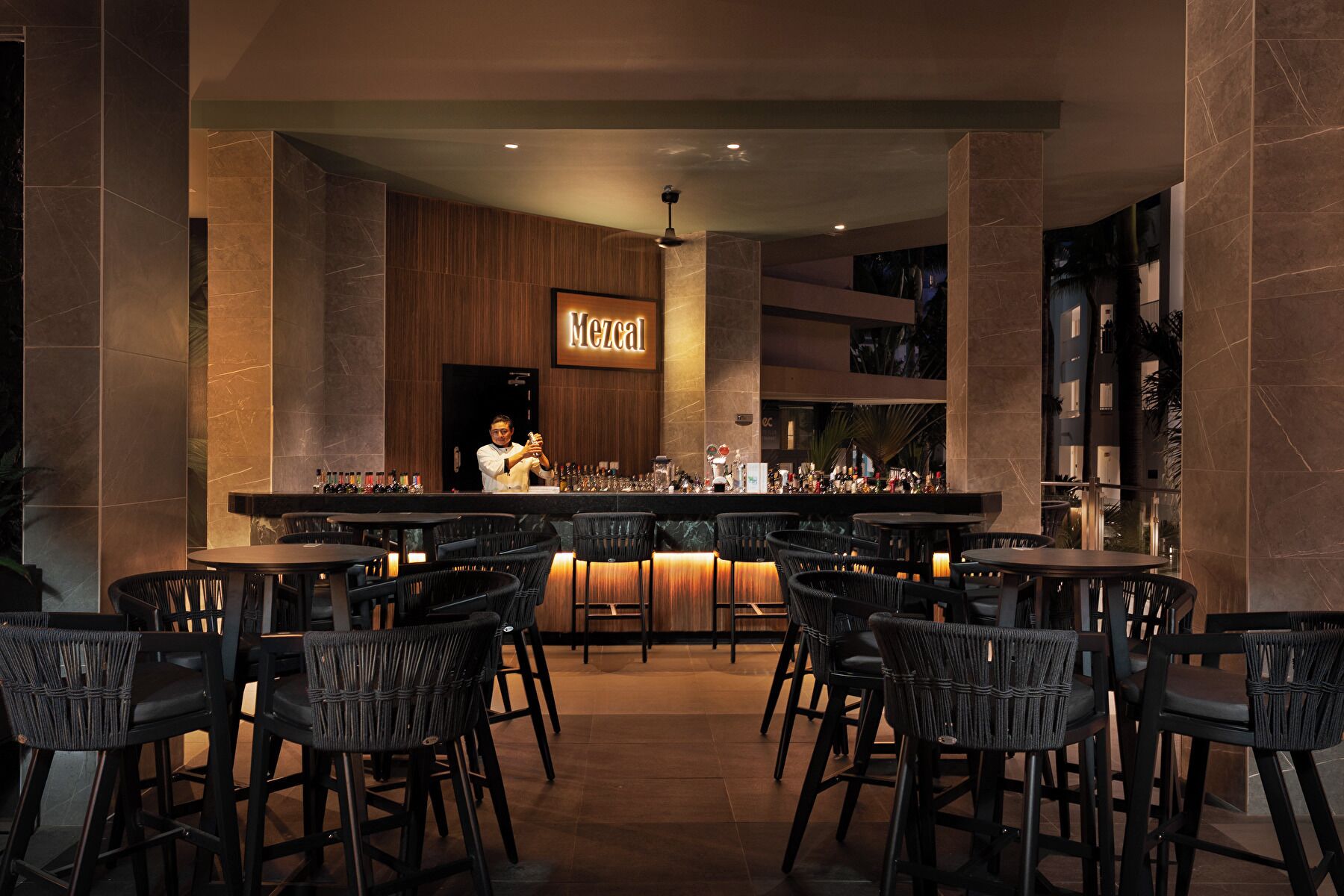 Un espace bar avec un barman, plusieurs tables et un comptoir.