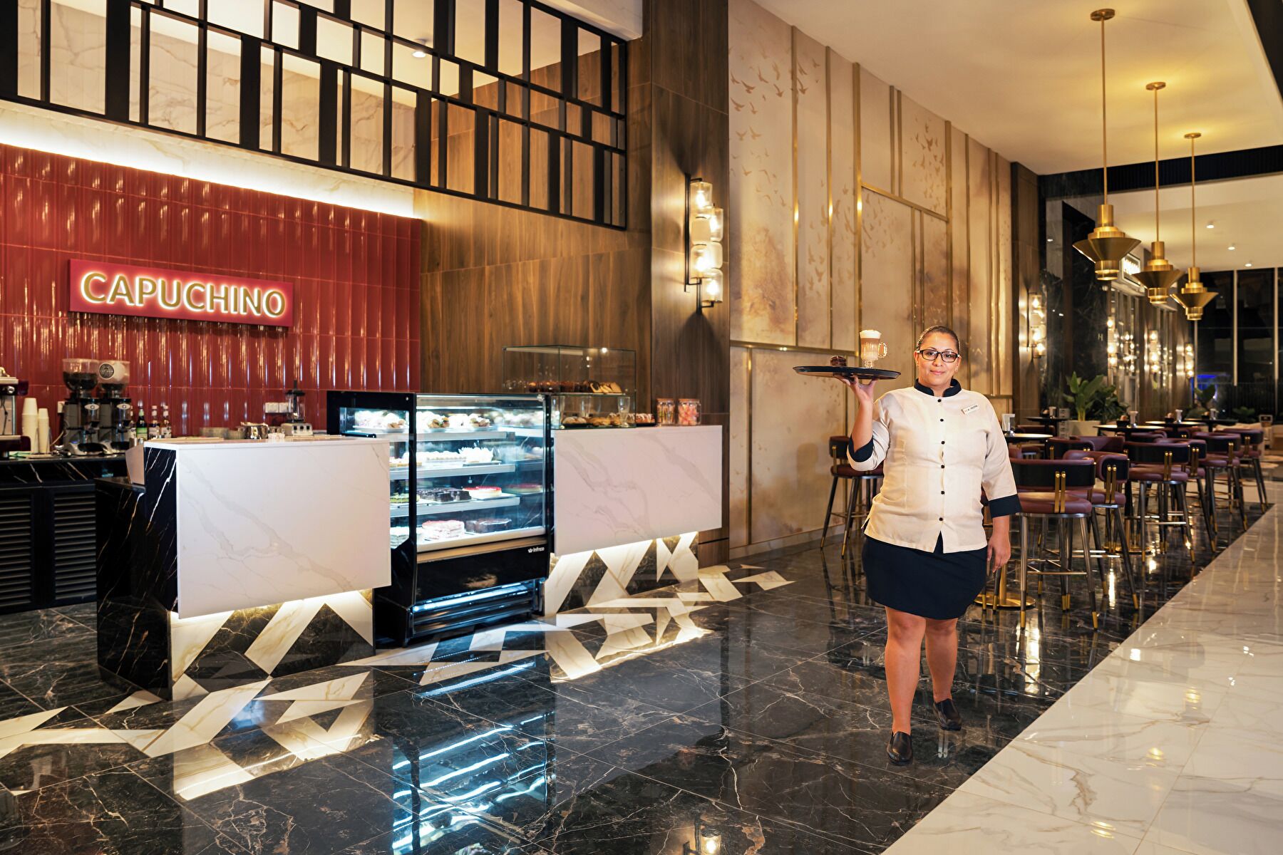 A hotel lobby with a Capuchino coffee station, a reception desk, and a waiter holding a tray.