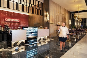 Un vestíbulo de hotel con una estación de café capuchino, una recepción y un camarero sosteniendo una bandeja.