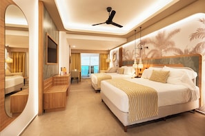 A hotel room with a large bed, a desk, a chair, a ceiling fan, and a view of the sea.