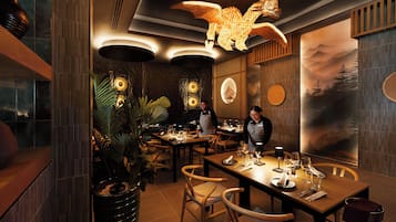 Interior de restaurante con mesas y sillas de madera, y una lámpara decorativa en el techo.