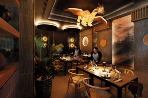 Interior de restaurante con mesas y sillas de madera, y una lámpara decorativa en el techo.
