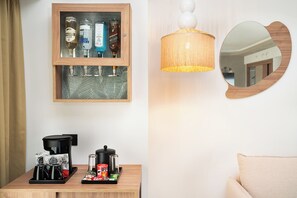 Una habitación con un aparador de madera, una mesa con equipo para preparar café, una lámpara colgante y un espejo redondo.